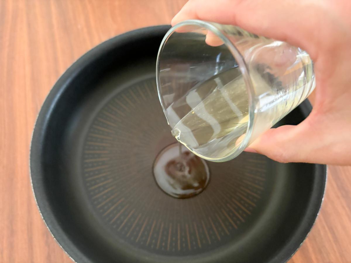 コップにたまった油をフライパンに注ぐ